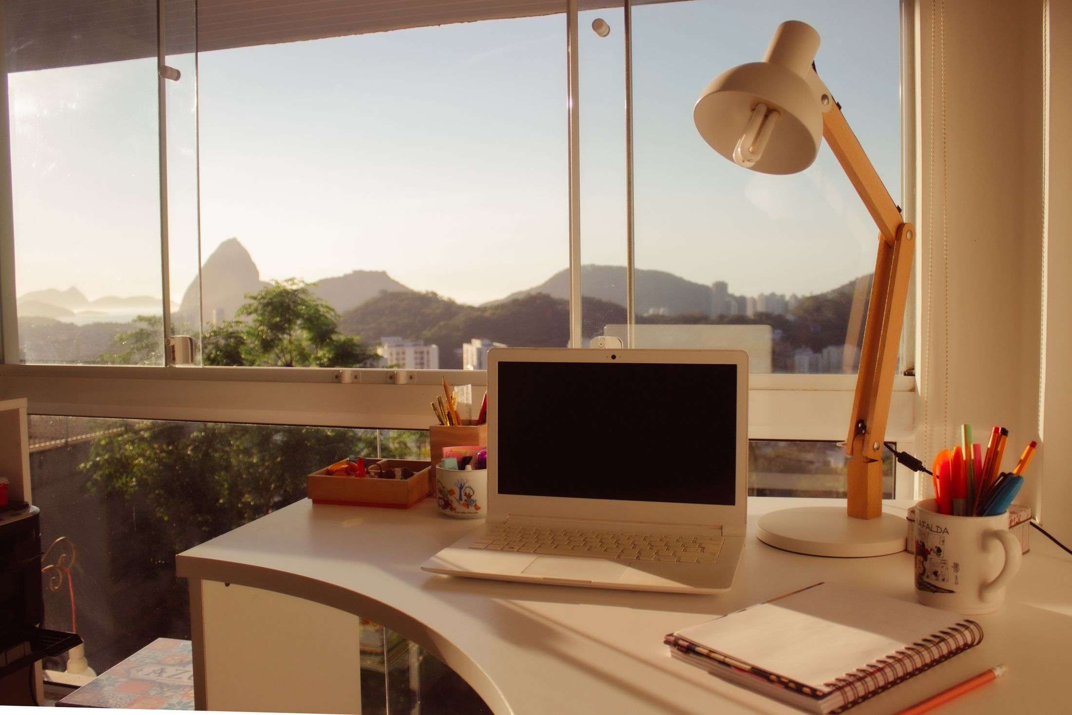 Schreibtisch mit Laptop vor einem Fenster mit Blick auf Berge und Meer
